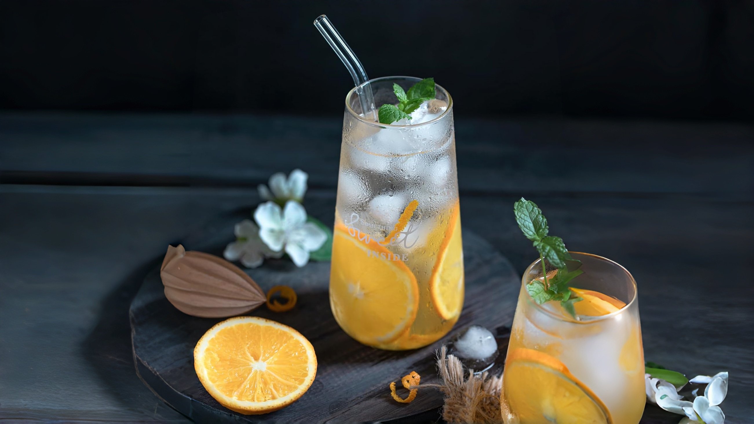 Piteno reusable glass straw inserted in a tall glass of ice water with condensation droplets, refreshing summer drink scene